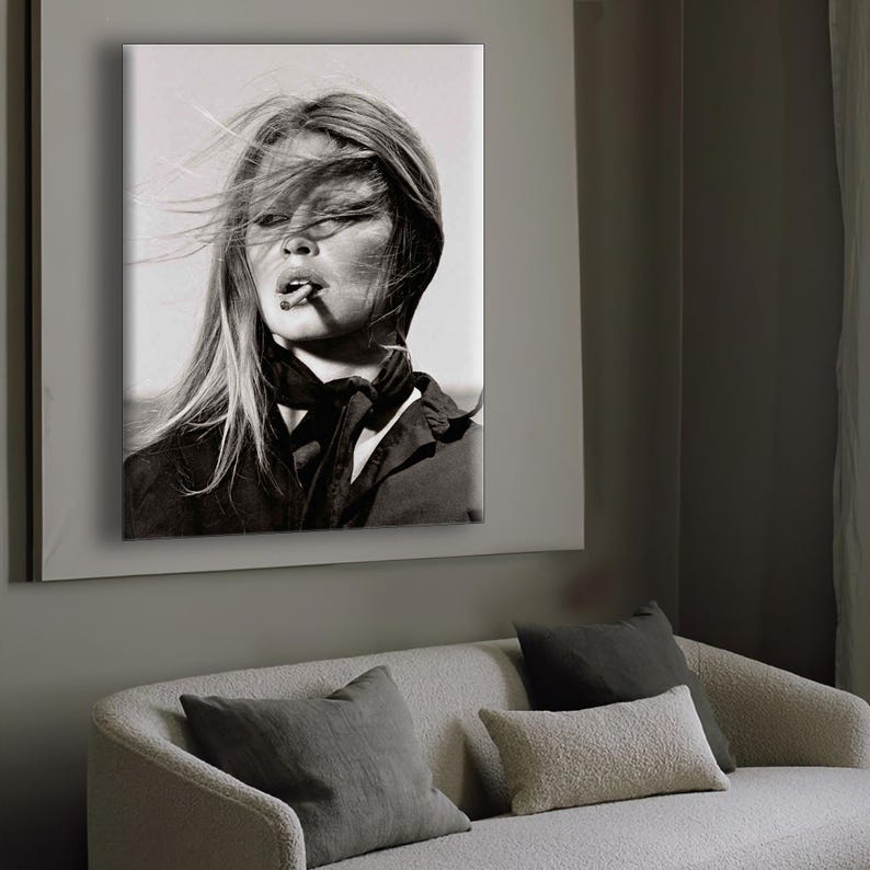 Puede incluir: Retrato en blanco y negro de una mujer con el pelo largo al viento, fumando un cigarrillo. Lleva un top oscuro y una bufanda. La imagen enmarcada est&aacute; montada en una pared sobre un sof&aacute; con cojines.