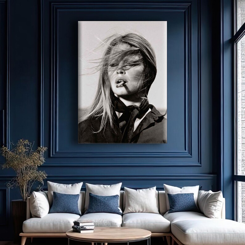 Puede incluir: Retrato en blanco y negro de una mujer con el pelo al viento, fumando un cigarrillo. Lleva una chaqueta oscura y una bufanda anudada al cuello. La imagen es una impresi&oacute;n en lienzo, expuesta en una pared azul oscuro.