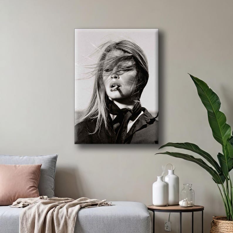 Puede incluir: Impresi&oacute;n en lienzo en blanco y negro de una mujer con el pelo largo al viento, fumando un cigarrillo. Lleva una bufanda y una chaqueta oscuras. La imagen es un retrato que captura un momento de estilo y desaf&iacute;o.