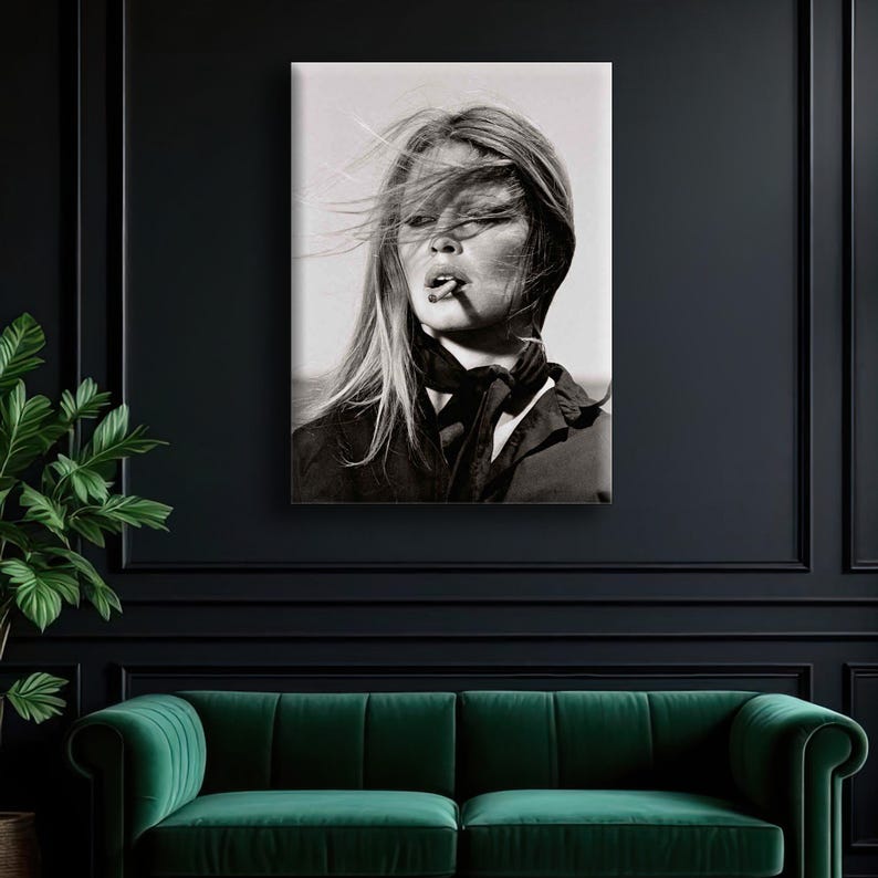 Puede incluir: Retrato en blanco y negro de una mujer con el pelo largo al viento, fumando un cigarrillo. Lleva un top oscuro y una bufanda. La imagen se muestra en un lienzo, montado en una pared oscura sobre un sof&aacute; de terciopelo verde.