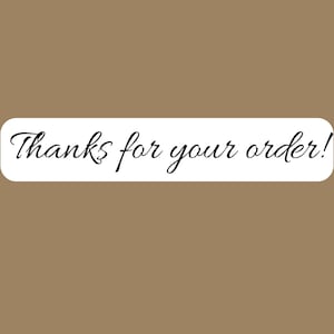 May include: A rectangular white sticker with rounded corners featuring the black cursive text Thanks for your order! centered on the surface. The sticker is presented against a solid, plain, light brown background color.