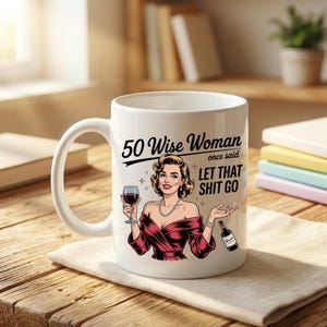 May include: White ceramic mug featuring a retro illustration of a woman in a red dress holding a wine glass and bottle. The mug has the text "50 Wise Woman once said LET THAT SHIT GO". A fun gift for a milestone birthday.