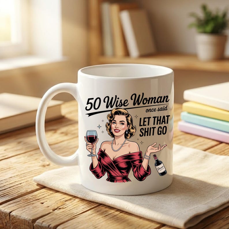 May include: White ceramic mug featuring a retro illustration of a woman in a red dress holding a wine glass and bottle. The mug has the text "50 Wise Woman once said LET THAT SHIT GO". A fun gift for a milestone birthday.