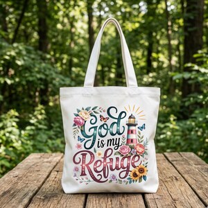 May include: A white canvas tote bag featuring a colorful graphic print with the text "God is my Refuge". The design includes a red and white striped lighthouse, various blooming flowers in shades of pink, yellow, and blue, and small butterflies.