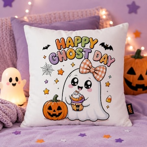 May include: A white square throw pillow featuring a colorful graphic of a ghost wearing an orange and white checkered bow, holding a cupcake. The text reads Happy Ghost Day, surrounded by a jack-o'-lantern, a spider web, bats, and stars.