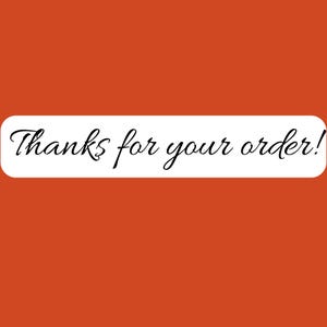 May include: A rectangular white sticker with rounded corners set against a solid burnt orange background. The text Thanks for your order! is printed in the center in a black, elegant, cursive script font, clearly legible across the white surface.