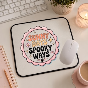 May include: A rectangular mouse pad with a black border and a central scalloped circular graphic. The graphic features the text "SUNNY DAYS SPOOKY WAYS" in orange, yellow, and black, surrounded by small pink flowers, yellow stars, and a black bat.