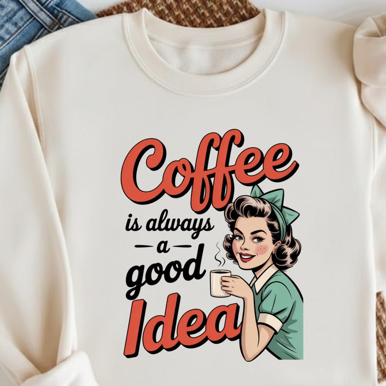 May include: Cream-colored sweatshirt with the text "Coffee is always a good Idea" in red and black. The graphic features a vintage-style illustration of a woman holding a coffee cup, wearing a green dress and a bow.