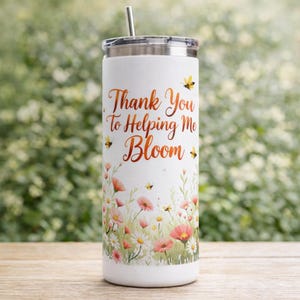 May include: White stainless steel tumbler with a floral design and the text "Thank You To Helping Me Bloom" in copper-colored script. The tumbler features a silver lid and straw, with illustrations of bees and flowers.