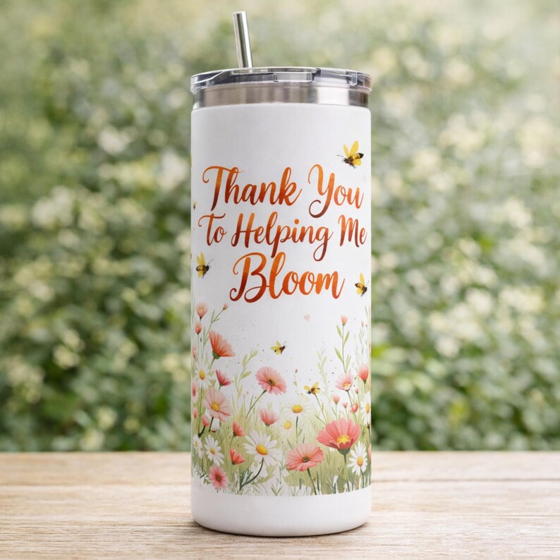 May include: White stainless steel tumbler with a floral design and the text "Thank You To Helping Me Bloom" in copper-colored script. The tumbler features a silver lid and straw, with illustrations of bees and flowers.