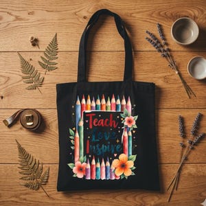 May include: Black tote bag with a colorful pencil design and the words "Teach Love Inspire". The bag features a floral design and is made of a durable fabric. Perfect for teachers or anyone who loves to inspire.