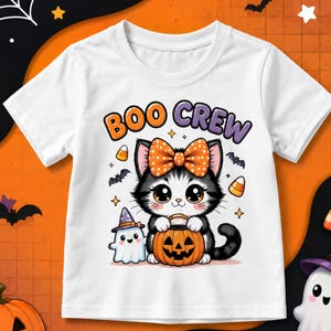 May include: A white short-sleeve t-shirt featuring a graphic of a black and white kitten wearing an orange polka-dot bow, holding a jack-o'-lantern bucket. Next to the kitten is a small ghost wearing a purple hat. The text reads BOO CREW.