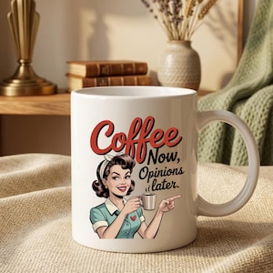 May include: White ceramic coffee mug featuring a retro illustration of a woman holding a coffee cup. The mug has the words "Coffee Now, Opinions later" in red and black lettering. The woman is wearing a blue dress and a white headband.