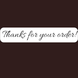 May include: A rectangular white sticker with rounded corners featuring the black cursive text Thanks for your order! centered on the surface. The sticker is presented against a solid dark brown background, highlighting the clear and legible lettering.