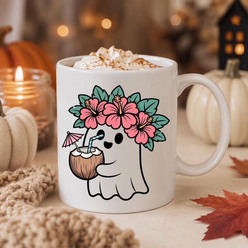 May include: A white ceramic mug featuring a graphic of a ghost wearing a pink hibiscus flower crown and holding a coconut drink with a straw and a small pink umbrella. The mug is filled with whipped cream topped with a dusting of brown spice.
