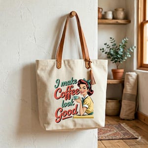 May include: Cream-colored tote bag with brown leather handles and a tassel. The bag features a retro illustration of a woman holding a coffee cup, with the text "I make Coffee look Good" in teal and red.