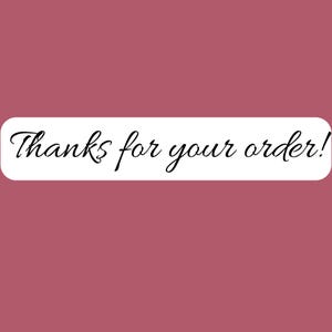 May include: A rectangular sticker with a white background and rounded corners featuring the black cursive text Thanks for your order! centered on the surface. The sticker is presented against a solid, muted mauve-colored background.