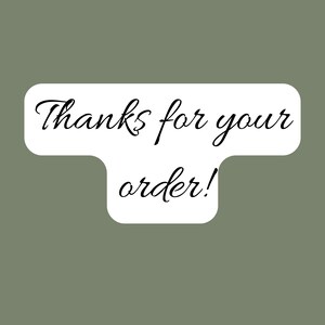 May include: A white sticker with rounded edges and the text "Thanks for your order!" in black cursive font. The sticker is set against a muted green background.