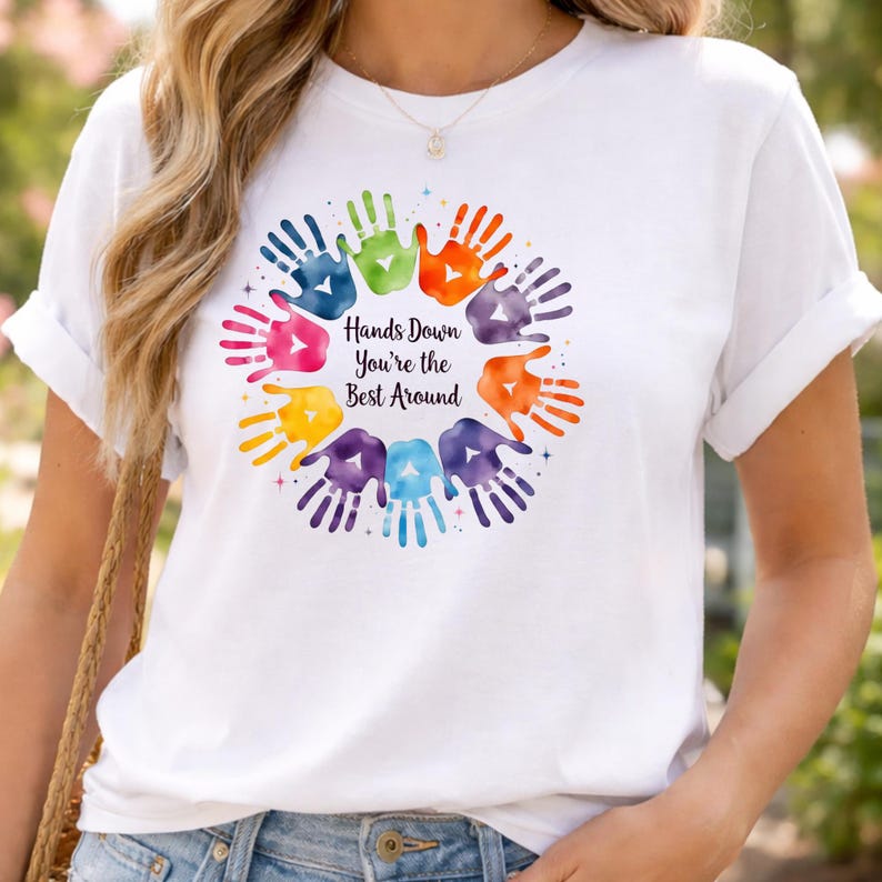May include: White t-shirt featuring a colorful handprint design arranged in a circle. The design includes handprints in various colors, such as pink, green, orange, and purple, with the text "Hands Down You're the Best Around".