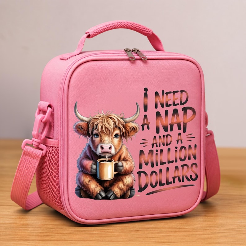 May include: A pink lunch bag with a top handle and a shoulder strap. The front features a graphic of a fluffy brown highland cow holding a mug, with the text "I NEED A NAP AND A MILLION DOLLARS" printed in a dark, stylized font next to the cow.