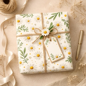 May include: A square gift box wrapped in white paper featuring a repeating pattern of white daisies with yellow centers and green leaves. The box is tied with brown twine, a small white daisy embellishment, and a blank rectangular gift tag.