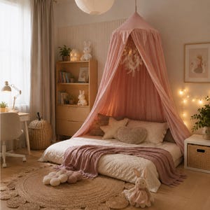May include: A dusty pink fabric bed canopy hangs from the ceiling over a low-profile bed. The bed features a white quilted coverlet, a dusty pink throw blanket, and several decorative pillows, including star-shaped and heart-shaped cushions.