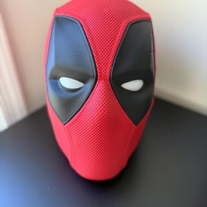 Peut inclure: Un masque intégral composé d'une base en tissu maille rouge vif texturé. Le masque présente de grands empiècements oculaires noirs angulaires à la surface mate et lisse, ainsi que des lentilles en maille blanche. La forme est arrondie.