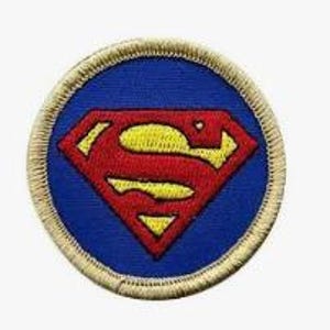 Könnte beinhalten: Ein kreisförmiger gestickter Aufnäher mit blauem Hintergrund und einem roten und gelben rautenförmigen Emblem in der Mitte. Der Aufnäher ist mit einem dicken, beigefarbenen gestickten Rand versehen, der das gesamte kreisförmige Design einrahmt.
