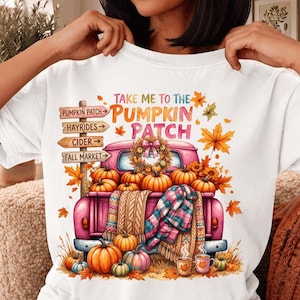 Peut inclure: Un t-shirt blanc avec un motif de pick-up rose rempli de citrouilles, d'une couverture à carreaux et de tasses. Le texte indique "TAKE ME TO THE PUMPKIN PATCH" avec un panneau en bois indiquant "PUMPKIN PATCH", "HAYRIDES", "CIDER" et "FALL MARKET".