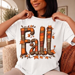 Peut inclure: Un t-shirt blanc à manches courtes avec le mot Fall écrit en grandes lettres style patchwork. Les lettres sont remplies de motifs orange, marron et gris, entourées de petites feuilles d'automne illustrées dans les mêmes tons.