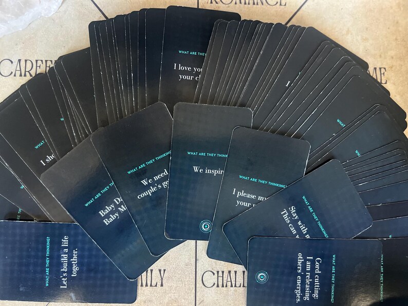 May include: A deck of black cards with white and teal text. The cards have rounded corners and feature phrases like "I love you" and "Let's build a life together." The deck is spread out on a light-colored surface.