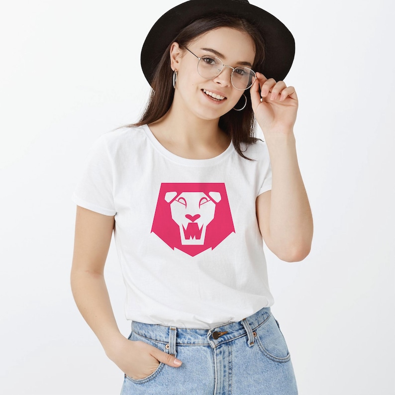 May include: White t-shirt featuring a pink lion graphic. The lion design is a stylized geometric shape with a white face and open mouth. The shirt is short-sleeved and made of a soft material.