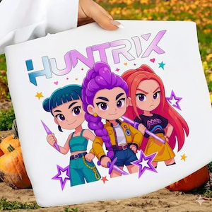May include: White tote bag featuring the word "HUNTRIX" in a gradient purple and blue font. The bag displays three cartoon characters with purple, red, and teal hair, each holding a weapon. The background includes stars and a pumpkin.