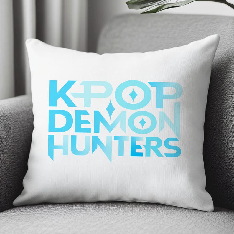 May include: White square pillow with the text "KPOP DEMON HUNTERS" in shades of blue. The text is centered and stacked, with diamond and star-like shapes incorporated into the design. The pillow is on a gray armchair.