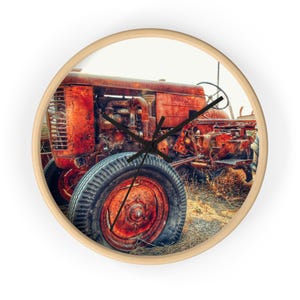 May include: Round wall clock featuring a vintage red tractor. The clock face displays the tractor's rusty details, including the tire, engine, and steering wheel. The clock has a light wood frame and black clock hands.