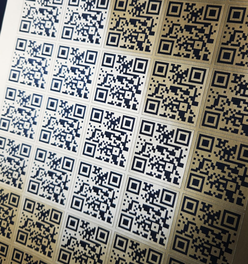 May include: Close-up of a sheet of gold-colored stickers printed with multiple black QR codes. The codes are arranged in a grid pattern, each a unique square of black and white pixels.