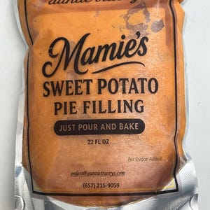 May include: A sealed package of Mamie's Sweet Potato Pie Filling. The orange filling is visible through the clear plastic. Text on the package includes "auntie tracey's", "SWEET POTATO PIE FILLING", and "JUST POUR AND BAKE". The package contains 22 fl oz.