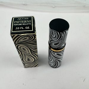 May include: An Avon Patterns perfume rollette in a black and white paisley patterned box and matching cylindrical container. The box features the text AVON PATTERNS PERFUME ROLLETTE .33 FL. OZ. The container has a solid black cap and a gold band.