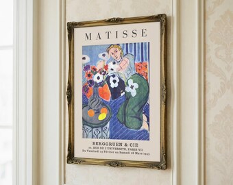 May include: A framed art print of a Matisse painting. The artwork shows a woman with flowers and fruit. The frame has an ornate gold finish. The print includes the name "MATISSE" and details about the gallery and exhibition dates.