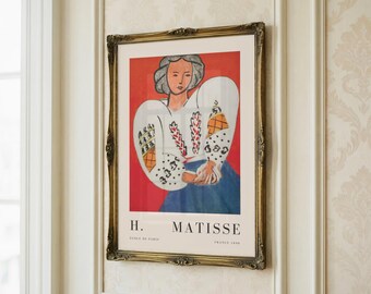 May include: A framed art print featuring a woman in a white blouse with colourful patterns, a blue skirt, and a red background. The print is labelled "H. Matisse" and is in a gold ornate frame, mounted on a wall.