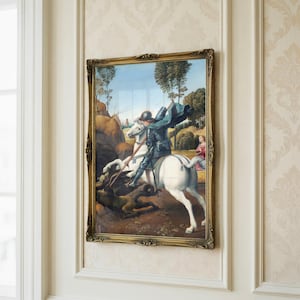 Puede incluir: Obra de arte enmarcada que representa a un caballero a caballo, lanceando a un dragón. La pintura tiene un marco dorado ornamentado y está montada en una pared con un patrón floral. El caballero lleva armadura y una capa azul, en un paisaje.