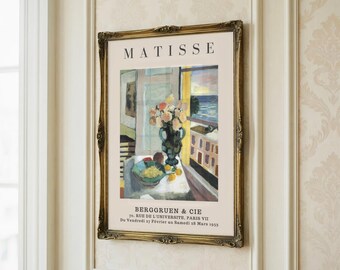 May include: A framed art print of a Matisse painting. The print features a still life with a vase of flowers, a bowl of fruit, and a window view. The frame is ornate and gold-coloured, and the text "MATISSE" is visible at the top.