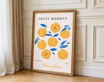 May include: A framed art print with a cream background, featuring yellow peaches and blue leaves. The print includes the text "FRUIT MARKET" and "Peaches". The frame is gold-colored. The artwork is displayed in a room with wooden flooring.