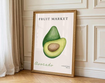 May include: A framed art print with a watercolour illustration of an avocado, whole and sliced. The print has the text "FRUIT MARKET" at the top and "Avocado" in cursive at the bottom. The frame is gold-coloured.