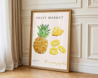 May include: A framed art print with a watercolour illustration of a pineapple, including a whole fruit, slices, and a wedge. The text "FRUIT MARKET" and "Pineapple" are in gold. The frame is gold.
