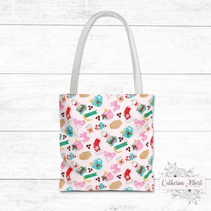 Op de afbeelding: Een lichtroze draagtas met een herhalend patroon van kerstthema-illustraties. Het patroon bevat koffiekopjes, koekjes, sokken en strikken. De tas heeft witte handvatten en de tekst "Catherine Albert Designs".