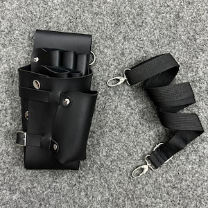 May include: Black leather barber tool holster with multiple compartments and a buckle closure. Includes a black adjustable strap with silver-tone metal clasps. The holster is designed to hold scissors and other grooming tools.