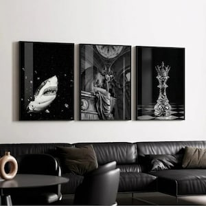 May include: Set of three framed black and white art prints. One features a shark, another a classical sculpture, and the third a crystal chess piece on a checkered board. The prints are displayed above a black leather sofa.