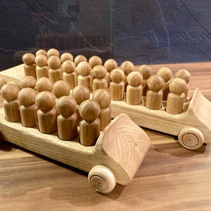 Könnte beinhalten: Zwei Holzspielzeugfahrzeuge, jedes mit einer Reihe kleiner Holzfiguren. Die Fahrzeuge sind aus hellem Holz mit abgerundeten Rädern und einer bootsähnlichen Form. Die Figuren sind ebenfalls aus Holz.