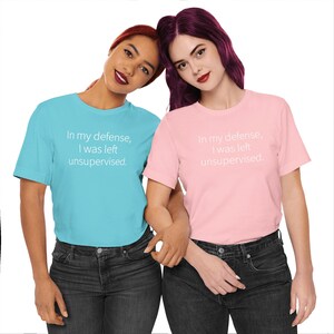 Peut inclure: Deux femmes portant des t-shirts assortis. L'un est bleu clair, l'autre rose. Les deux chemises portent l'inscription "In my defense, I was left unsupervised" en blanc. Elles portent toutes les deux des jeans d&eacute;lav&eacute;s fonc&eacute;s.